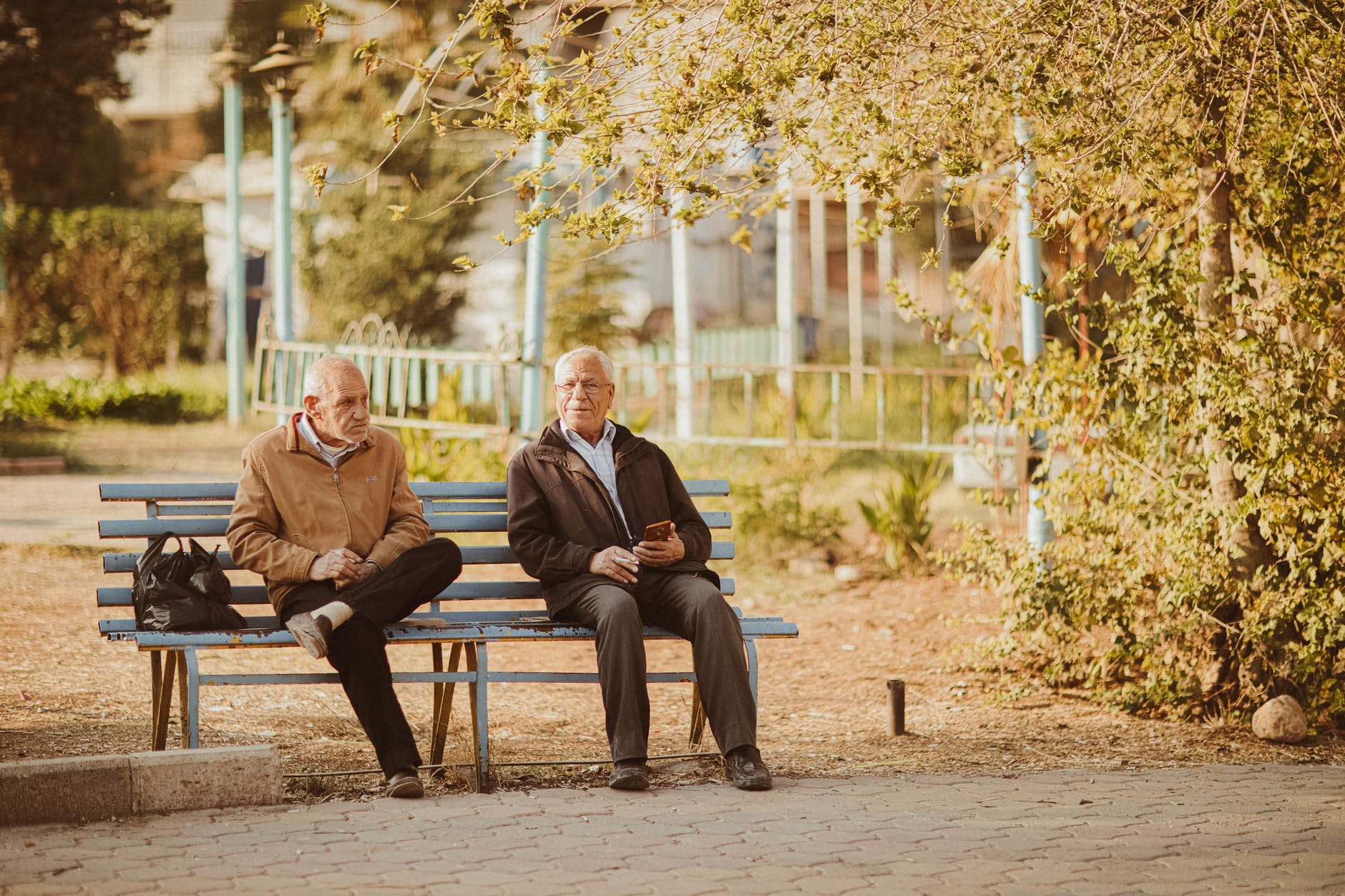 two old men sitting on bench in park in autumn